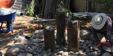 Person arranging stones and wooden posts outdoors in a garden or yard.