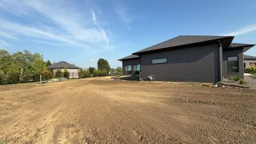 A modern house under construction with a large dirt yard and clear sky.