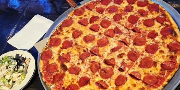 Large pepperoni pizza with a side salad on a dark table.