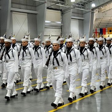Navy sailors marching in formation indoors.