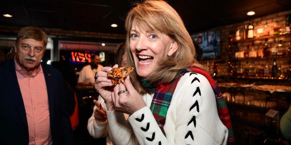 A woman happily eating pizza in a lively bar setting.