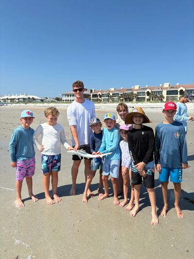 Group of kids holding a small shark on the beach.