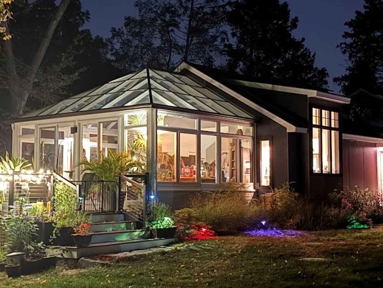 A cozy house illuminated at night with a glowing sunroom and garden lights.