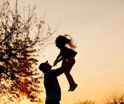 Silhouette of a man lifting a child against a sunset sky.