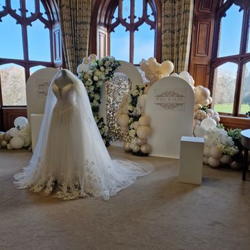 A bridal gown before an ivory balloon-floral backdrop, radiating romance and sophistication
