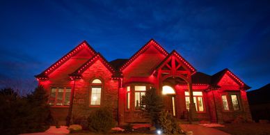 Stone home lit in solid red for game day with permanent JellyFish roofline lights