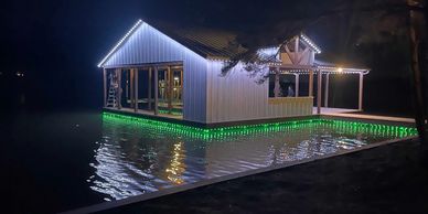 Lakeside boathouse with permanent white roofline lighting and green dock edge lights reflecting on t