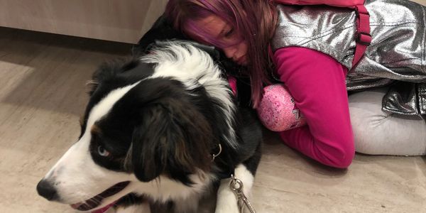Girl hugging a black and white dog on the floor.