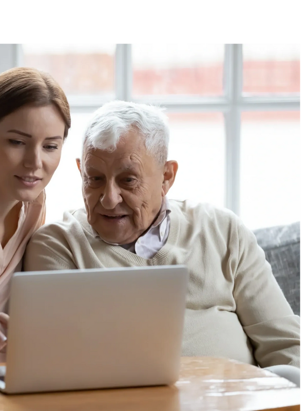 Young woman helps elderly man use a laptop together at home.