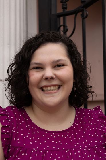 Smiling woman with curly hair wearing a purple polka dot top.