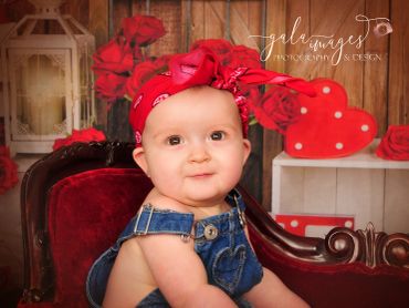Adorable baby in denim overalls with a red headband, sitting on a vintage chair.
