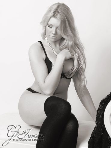 Black and white photo of a woman in lingerie and stockings posing thoughtfully.