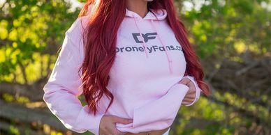 Woman wearing a pink hoodie with "DroneLyFans.ca" logo outdoors.