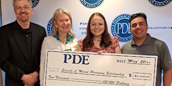 Four people holding a large $2,000 scholarship check from PDE Pharmacy.