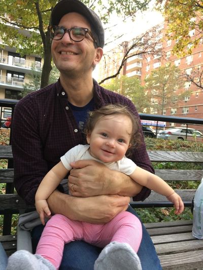 Andrew Gardner gleefully holding his daughter on a park bench.