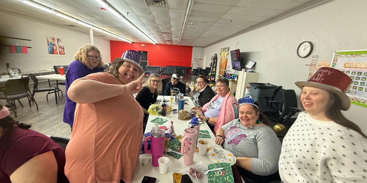 Group celebrating New Year's Eve with hats and smiles around a festive table.