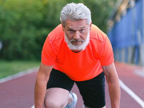 Older man in starting stance on running track.