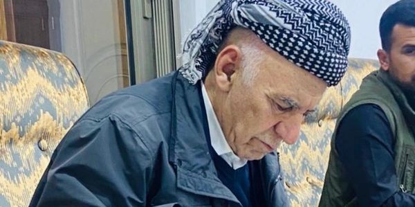Elderly man in traditional headwear sitting indoors, focused on writing.