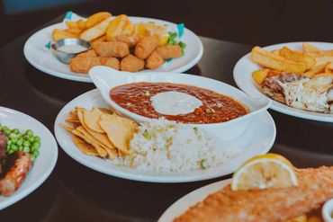 A table with plates of food including chili, rice, chips, chicken nuggets, and fries.