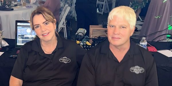 Two event staff members sitting at a control table during a lively gathering under a large tent.