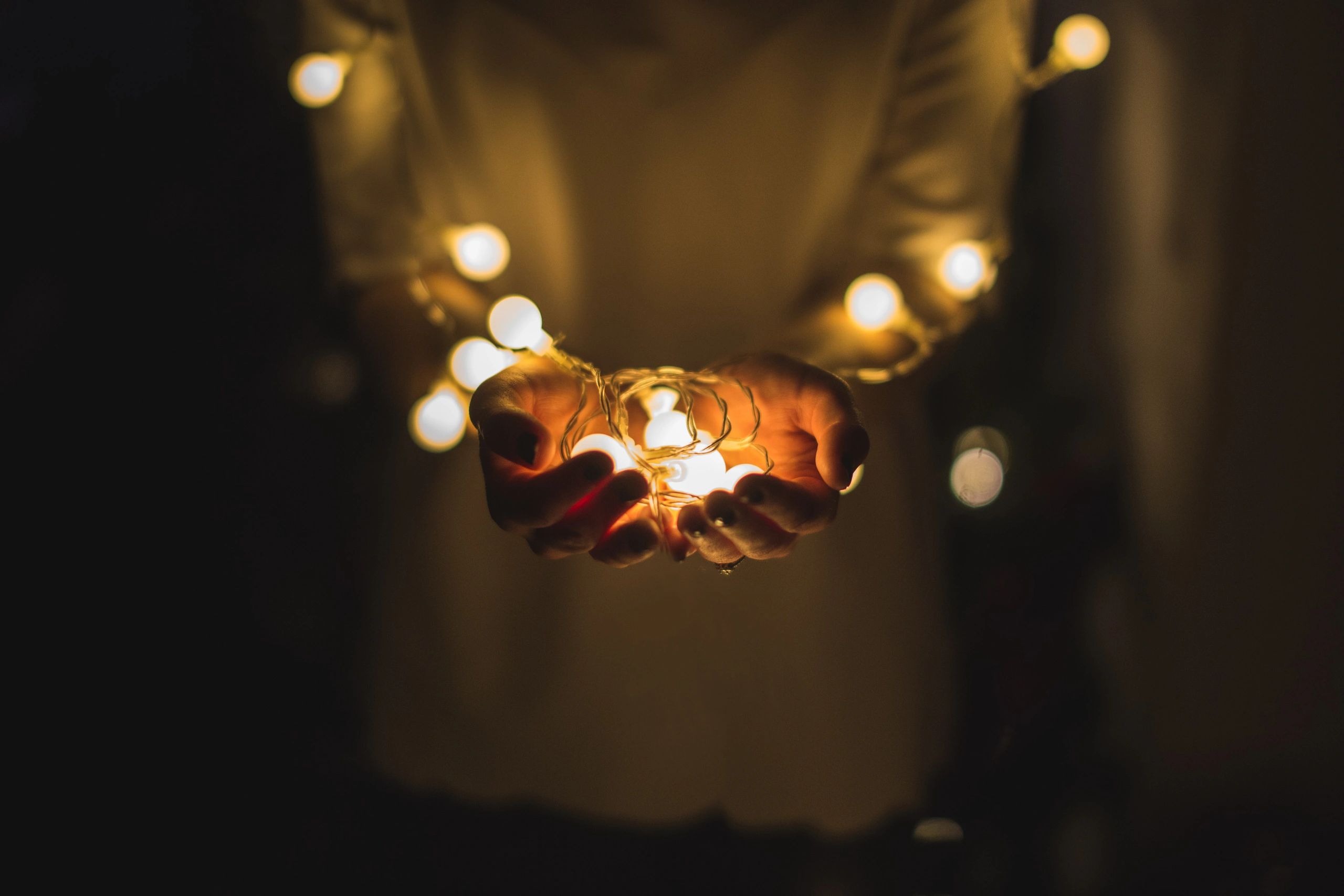 Hands gently holding glowing string lights in a dark setting.