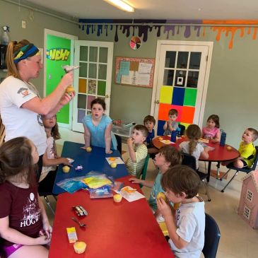 Teacher instructs kids at colorful classroom tables.