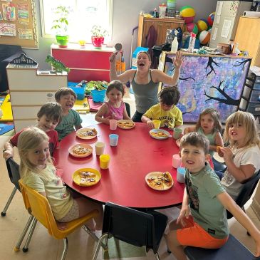 Group of children and an adult enjoying food at a table.