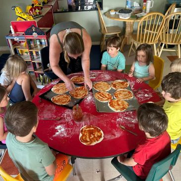 Children and adult making pizzas around a table.