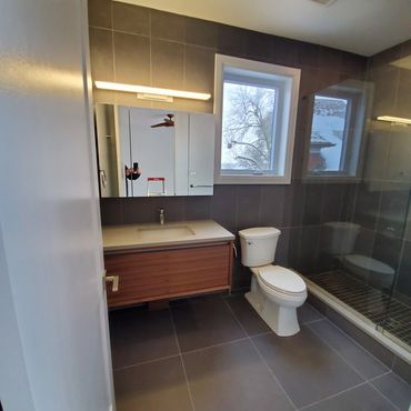 Modern grey tiled 3 piece washroom, with a walnut floating vanity with a MCM feel. Custom shower