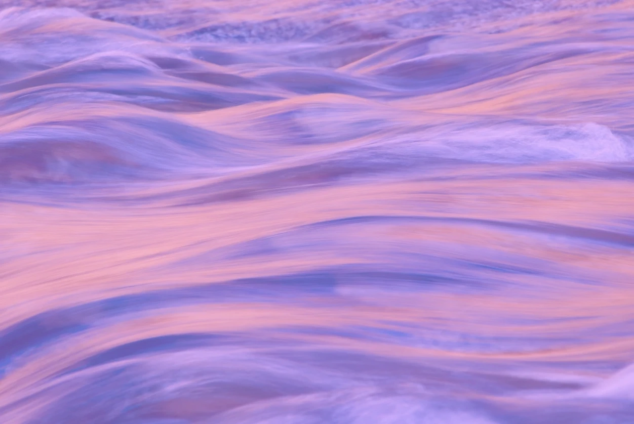 Soft waves in a purple and pink tinted water surface.