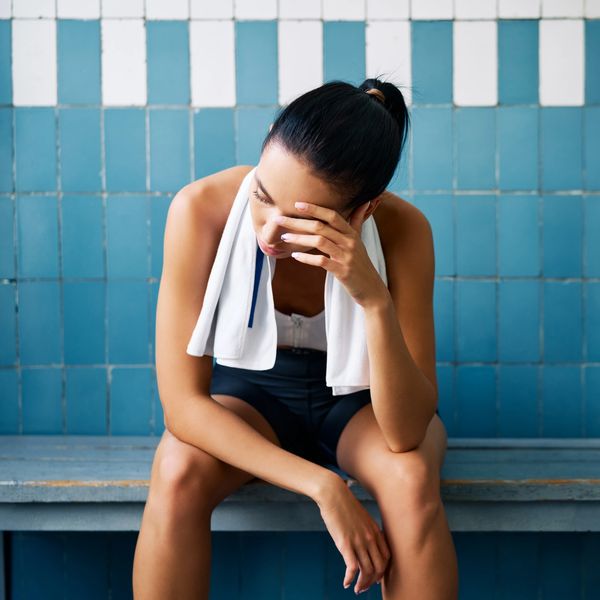 Tired woman resting on a bench after exercise, holding her face with a towel around her neck.