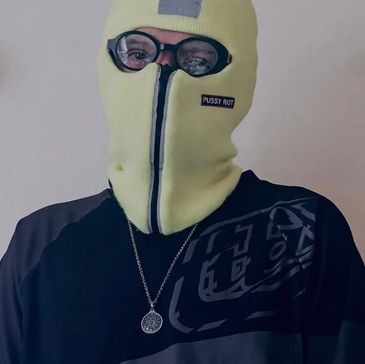 Person wearing a yellow balaclava with glasses and a pendant necklace.