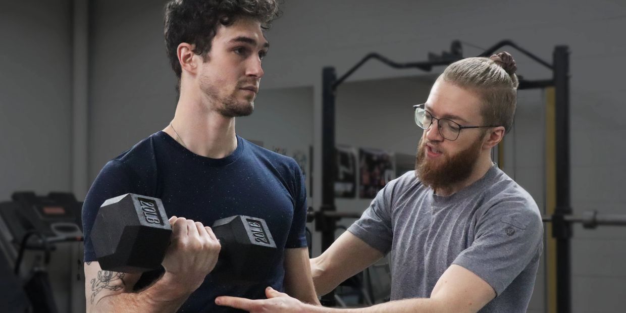 Trainer working with client. The client is doing dumbbell curls, while the trainer feels the clients