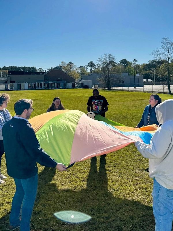Group of people playing with a colorful parachute outdoors on a sunny day.