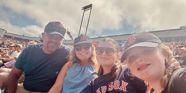 Family enjoying a sunny day at a Red Sox baseball game.