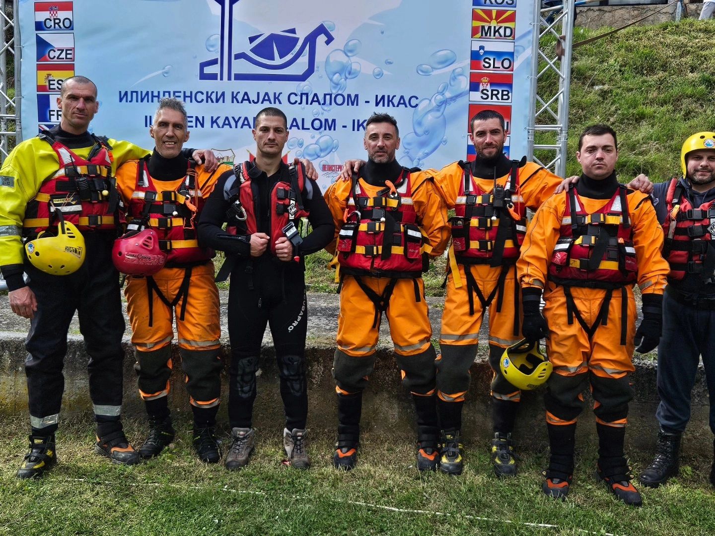 Group of seven men in kayak rescue gear posing in front of a banner.