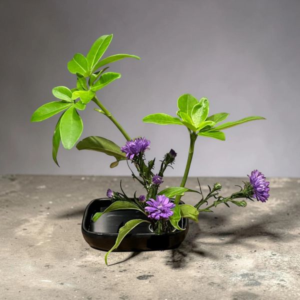 Elegant ikebana with green leaves and purple flowers.