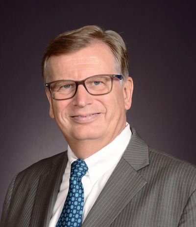 Professional middle-aged man in glasses, suit, and patterned tie smiles warmly.