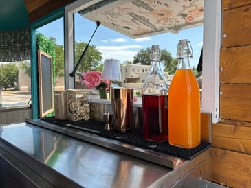 A stylish drink preparation setup with bottles, glass containers, and a flower on a counter by a window.