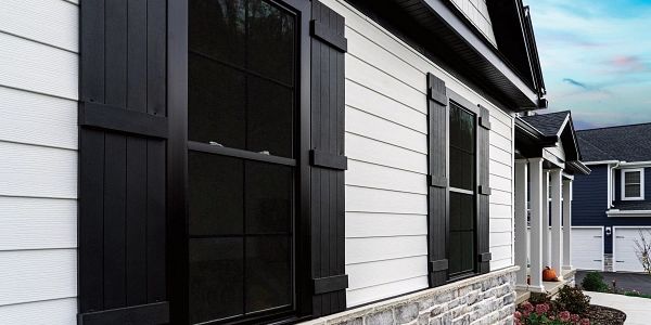 White house exterior with black window shutters and stone foundation under a clear sky.