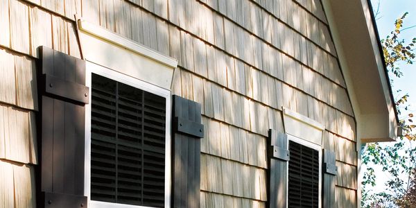 Close-up of house exterior with wooden shingles and black window shutters.