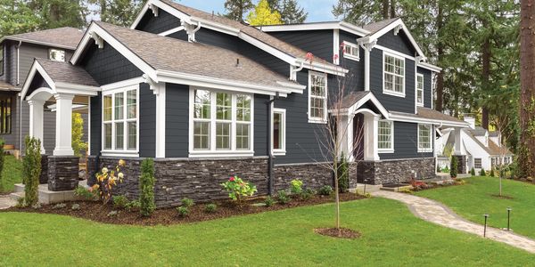 Modern two-story house with dark siding and stone accents surrounded by greenery.