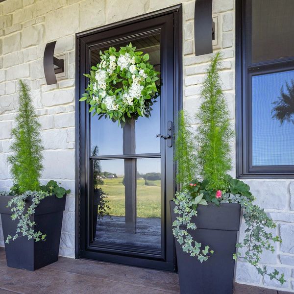 Black door with a green and white floral wreath and matching potted plants.