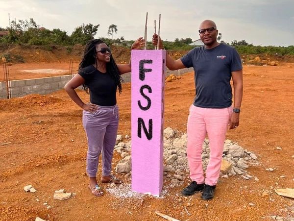 Two people standing next to a pink concrete pillar with 'FSN' written on it.