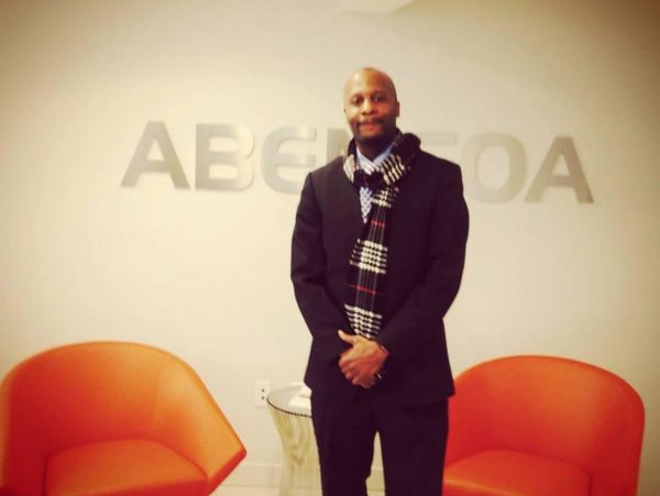 Man in suit and scarf standing between two orange chairs in front of a sign.