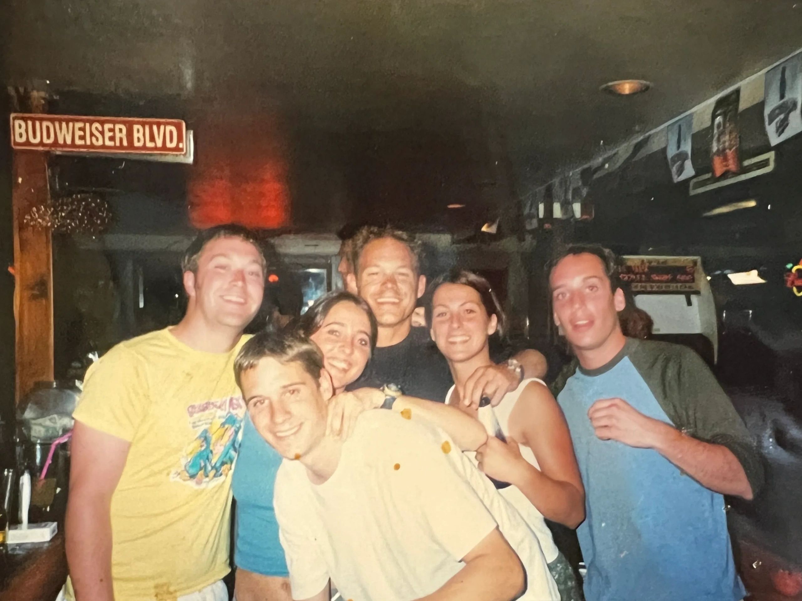Group of six friends smiling indoors under a Budweiser Blvd sign.