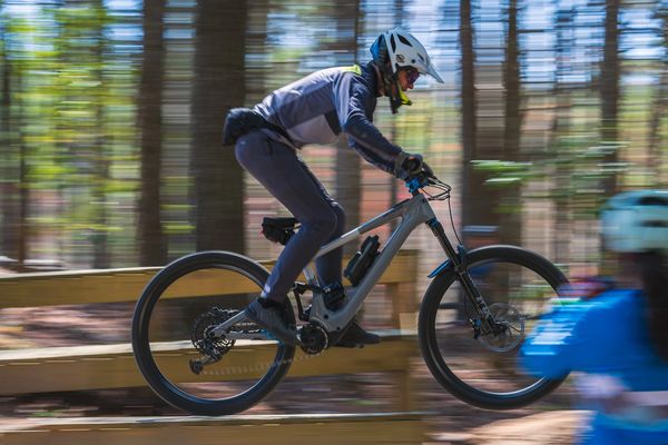 Mountain biker being coached on how to ride drops off of a small wooden feature.