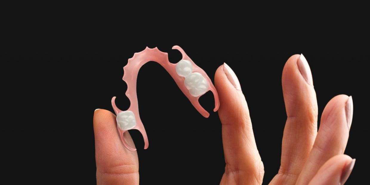 Hand holding a partial denture against a black background.