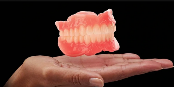 A hand holding a set of dentures against a black background.