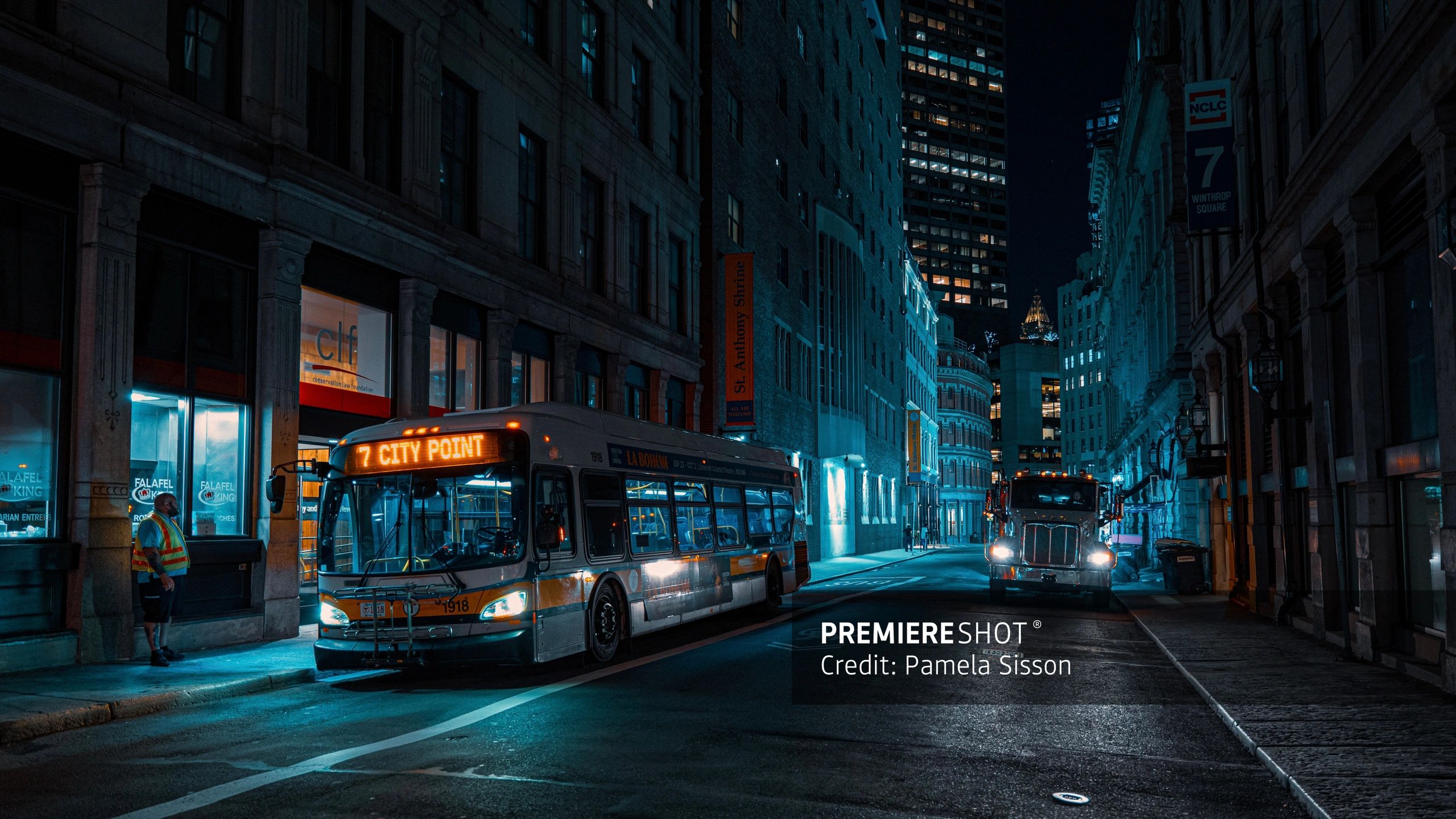 Night city street with a bus and a truck under blue lighting.